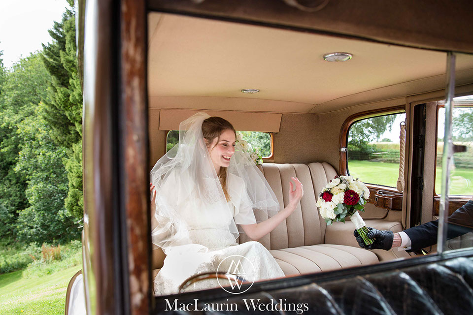 a happy bride in the wedding car recieving her bouquet from the chauffeur