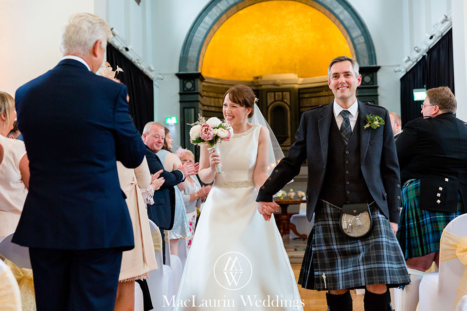 a happy bride and groom leaving the ceremony at the rivers suite napier university 