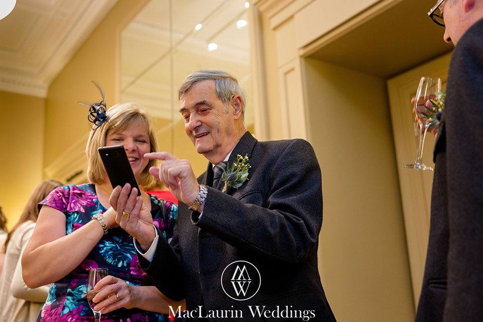 guests enjoying some images on a smartphone during the the drinks reception at the rivers suite napier university 