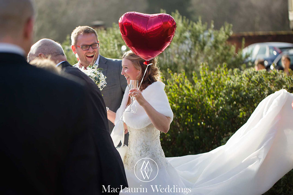 a happy bride walks with guests holding a loveheart baloon