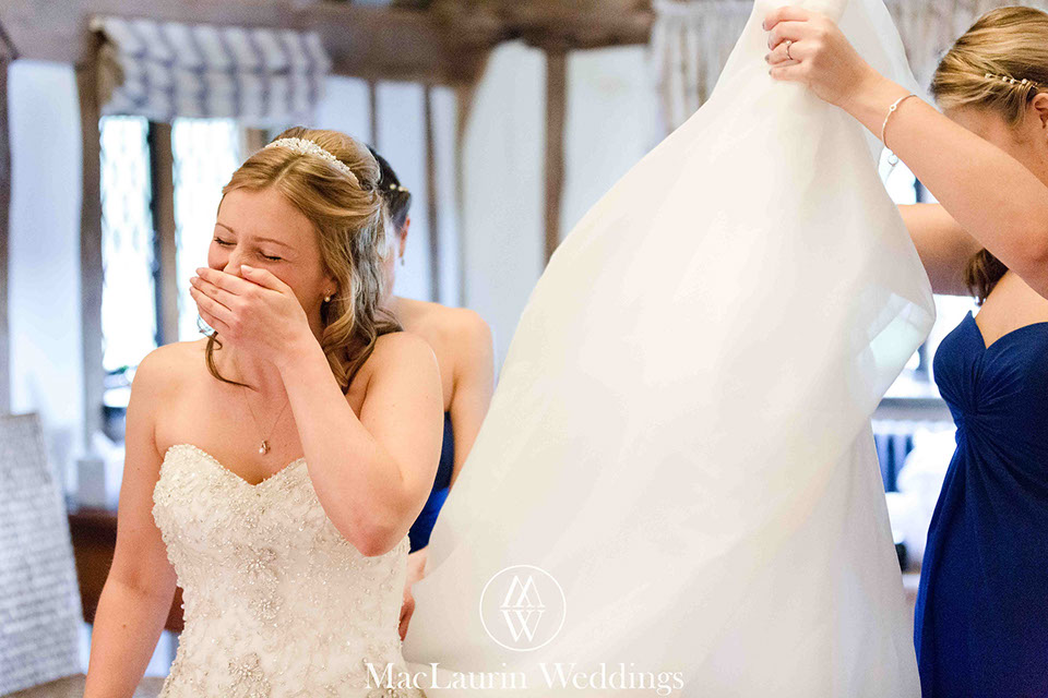 bride laughs as she is getting into her dress before wedding